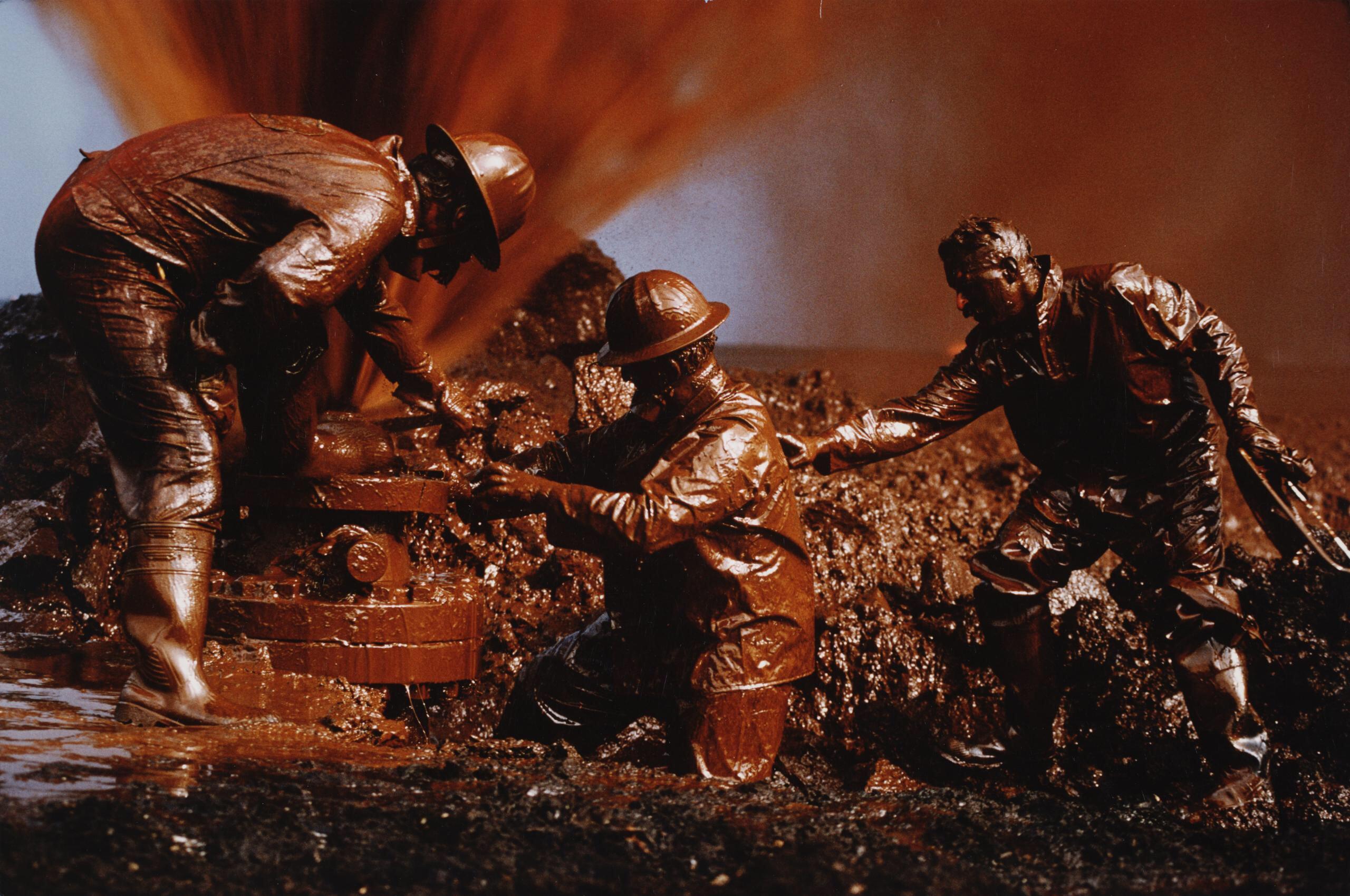 Firefighters covered in crude oil work to cap a wellhead in Kuwait